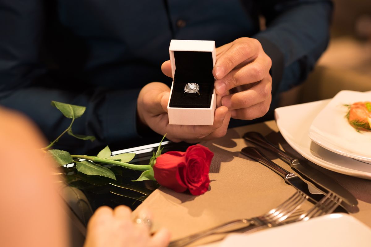 Man proposing with a diamond engagement ring accompanied by a red rose