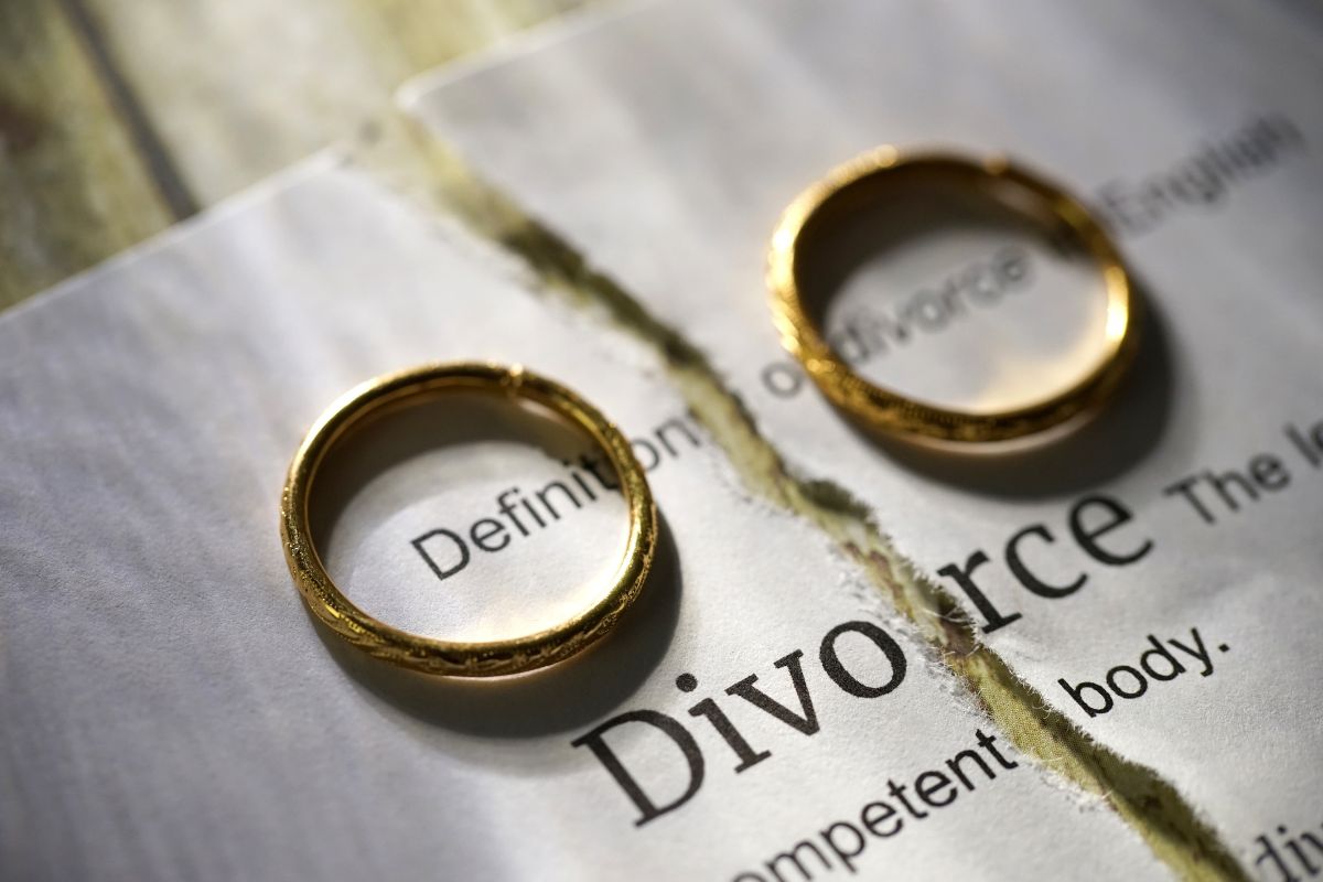 Two diamond engagement rings lie on a torn piece of paper with the word divorce written on it