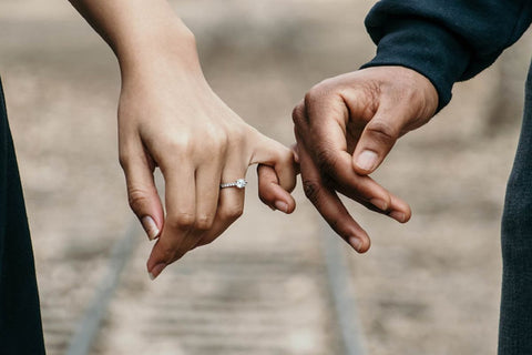 Two hands holding each other and the womans hand wearing a promise ring