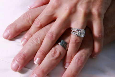 Two hands wearing wedding band and an engagement ring