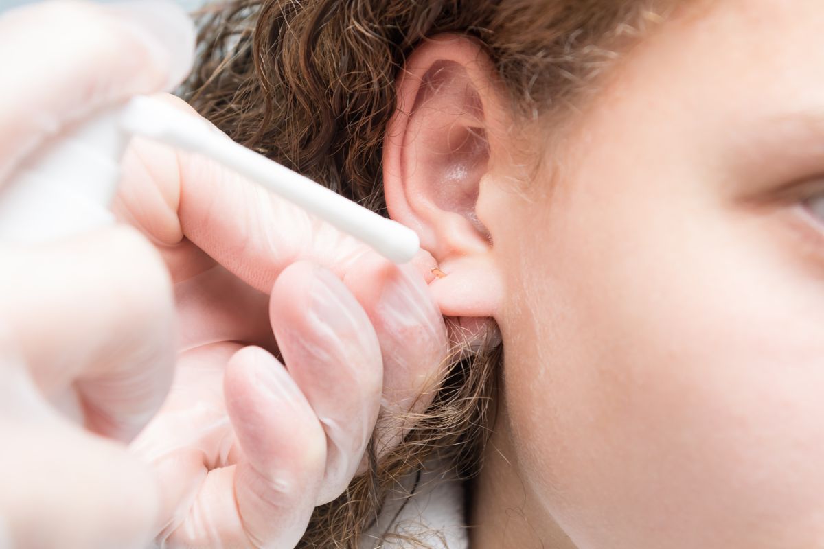 Woman applying saline solution after removing butterfly back earrings