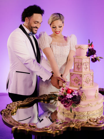 Groom in white jacket with black lapels, and bride, cutting pink tiered cake.