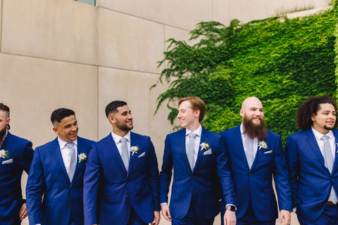 Close up of men in bridal party, smiling and looking at each other in a row.