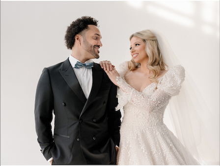 Groom on left, wearing a black double breasted suit, with bride on right, both smiling