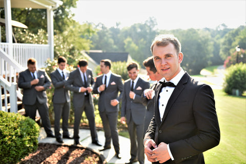 Groom standing on right, closer than the rest of his groomsmen, with green background