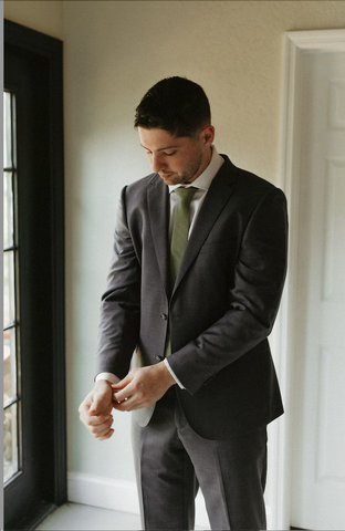 Man adjusting sleeve of dark grey, single breasted suit.