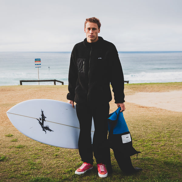 Rusty Australia team rider Letty Mortensen standing at beach holding surfboard and wetsuit
