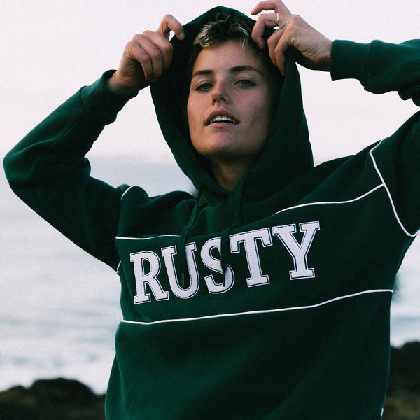 Model Charlotte Rose Beers posing at the beach wearing the Rusty Line Oversized Hooded Fleece in colour green gables.
