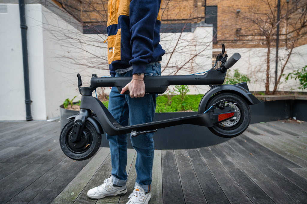 Person carrying a folded Riley Rs1 electric scooter