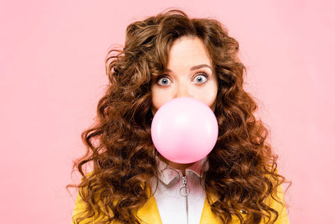 young curly haired woman blowing a bubble with pink gum