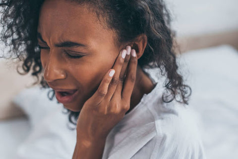 Young woman with dark curly hair holding her ear in pain.