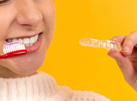 Close up of a young woman smiling while holding up a toothbrush and a mouth guard