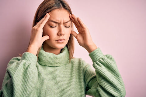 woman in a green turtleneck sweater holding her face in pain (tmj)
