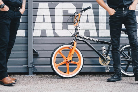 people wearing jeans beside an orange bicycle