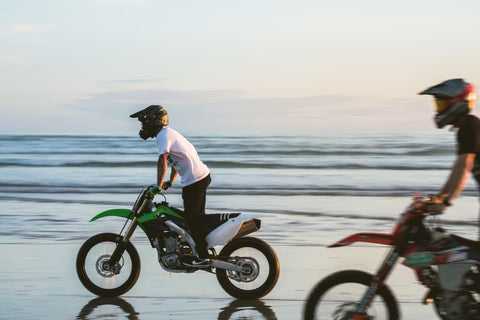 two men riding motorbikes on the beach