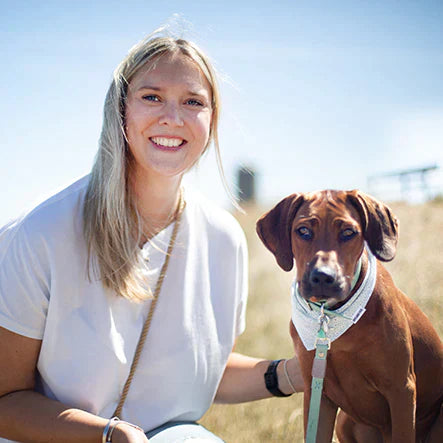 A smiling woman with a dog outdoors on a clear, sunny day.