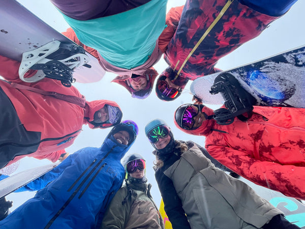 women in snowboard gear standing in a circle looking down at the camera