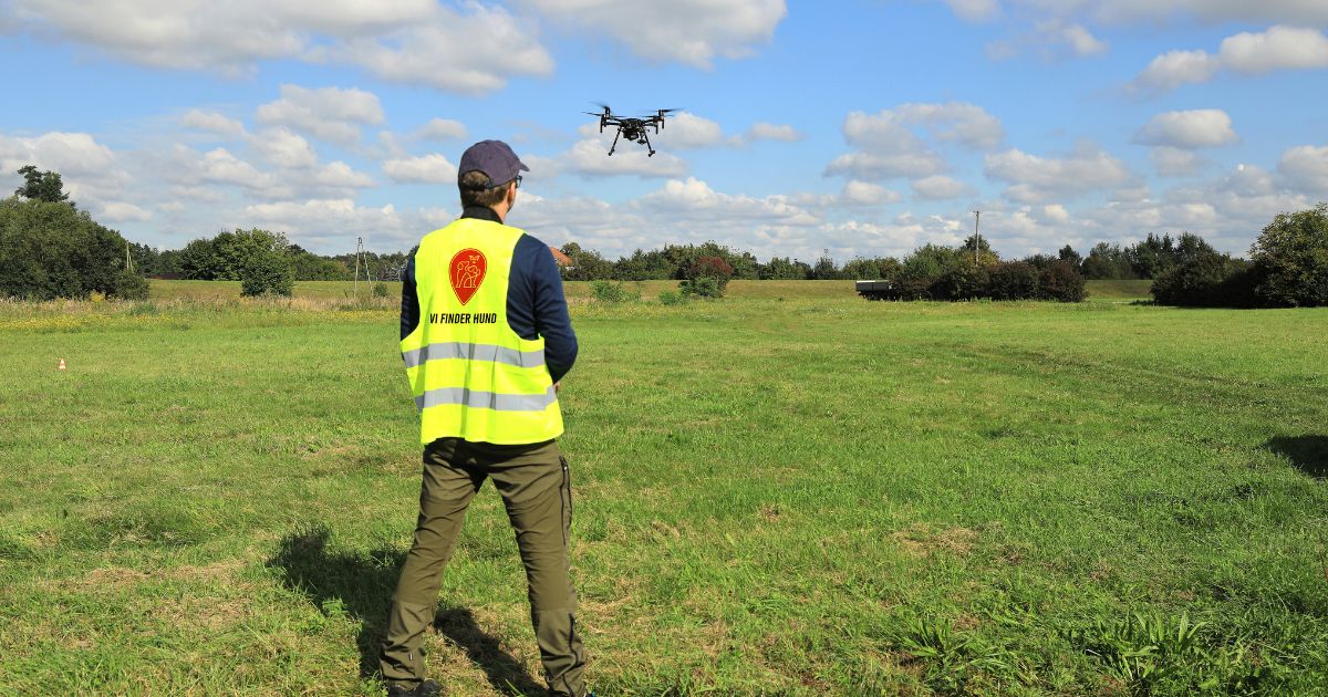 Mand med gul vest på en mark eftersøger hund med drone