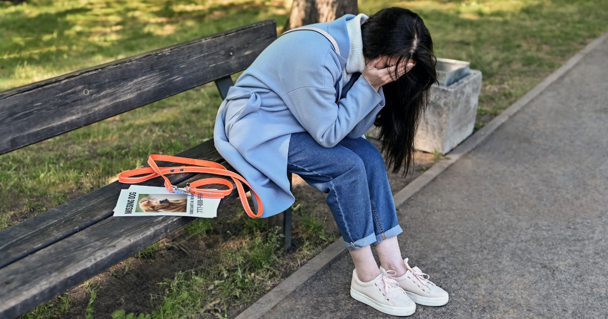 Trist kvinde på en bænk med flyers af en efterlysning af en hund liggende ved siden af