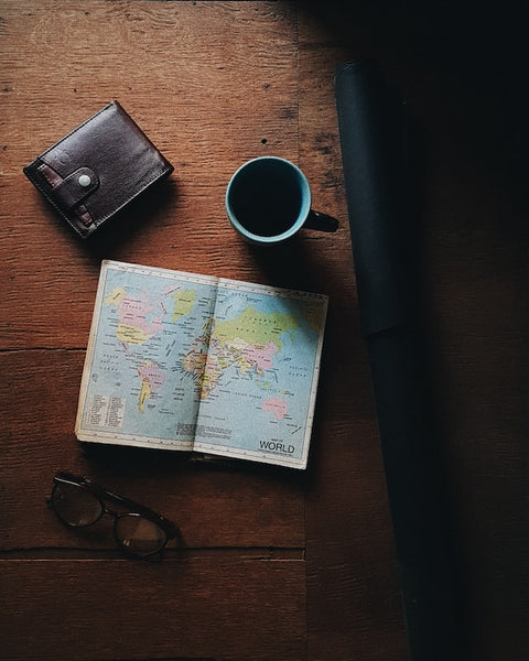 cup of black coffee next to a world atlas and a wallet on a dark mahogany table
