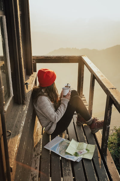 girl sitting on a fire lookout drinking coffee at sunrise next to world maps