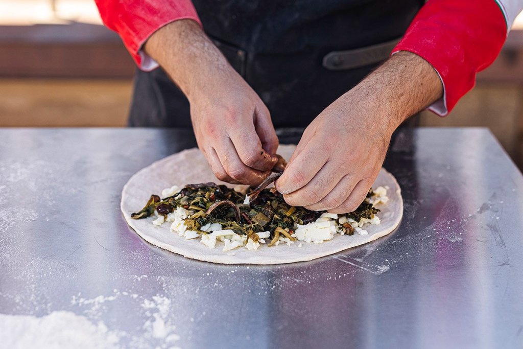  Two hands placing anchovies onto uncooked dough with escarole and provola on top of an Ooni Modular Table.