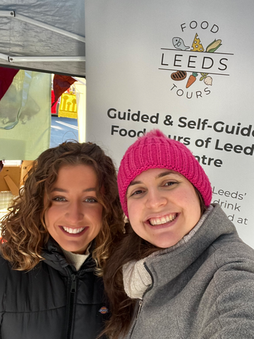 Georgia & Ellen stood in front of the Leeds Food Tours banner smiling at the camera