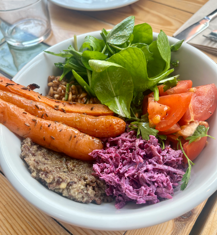 A salad bowl with brightly coloured leaves, carrots, red cabbage slaw, tomatoes and grains in a white bowl. At Eat Your Greens, one of the best vegetarian restaurants in Leeds.