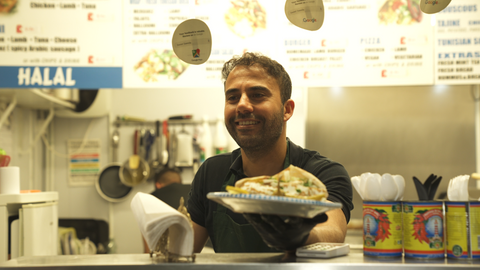 one of the best things to do in leeds is enjoy the street food. Image shows a man at a street food stall in Leeds market handing over a Tunisian sandwich