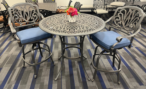 Silver-Metal cast aluminum bar table and 2 bar chairs with blue cushion on grey carpet.