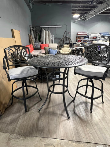 Grey metal flower pattern bar table surrounded by two bar chairs with grey cushions.