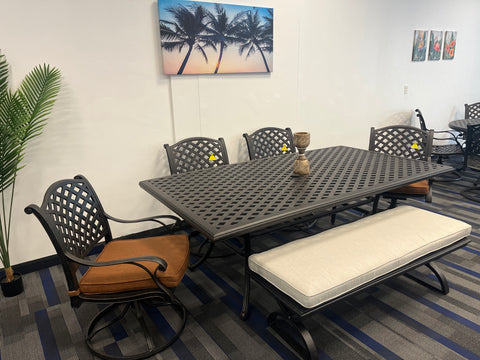 Dark cast aluminum rectangular table with 4 weave pattern chairs, and 1 bench.  Painting of palm trees on wall