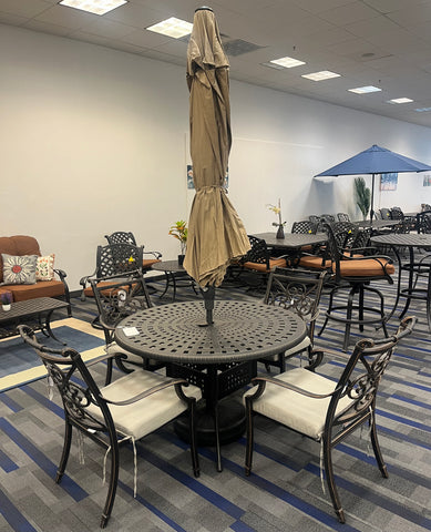 dark cast-aluminum round table with a closed umbrella in the center, surrounded by 4 ornate dining chairs.