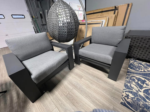 Two wide-armed grey metal club chairs with grey cushions.  Grey swinging egg chair in background.
