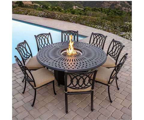 Oversized Firepit with fire lit in center, surrounded by black armless aluminum chairs.  Outside on concrete by swimming pool