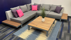 Patio Sectional with teak siding, and pink throw pillows on blue and grey carpet.