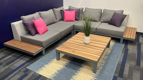 Fabric and teak sectional with pink and purple throw pillows and coffee table with a plant in the middle.