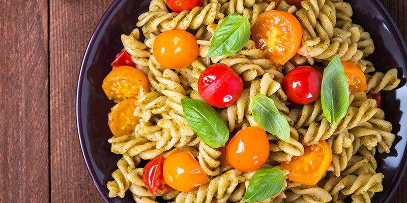 Fusilli pesto pasta salad with red and yellow tomatoes and fresh basil