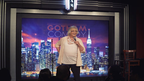 Trans comedian, Julia Scotti, on stage with microphone in hand