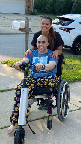 a young man and a woman pose behind the Companion, a scooter-like device attached to the front of his wheelchair