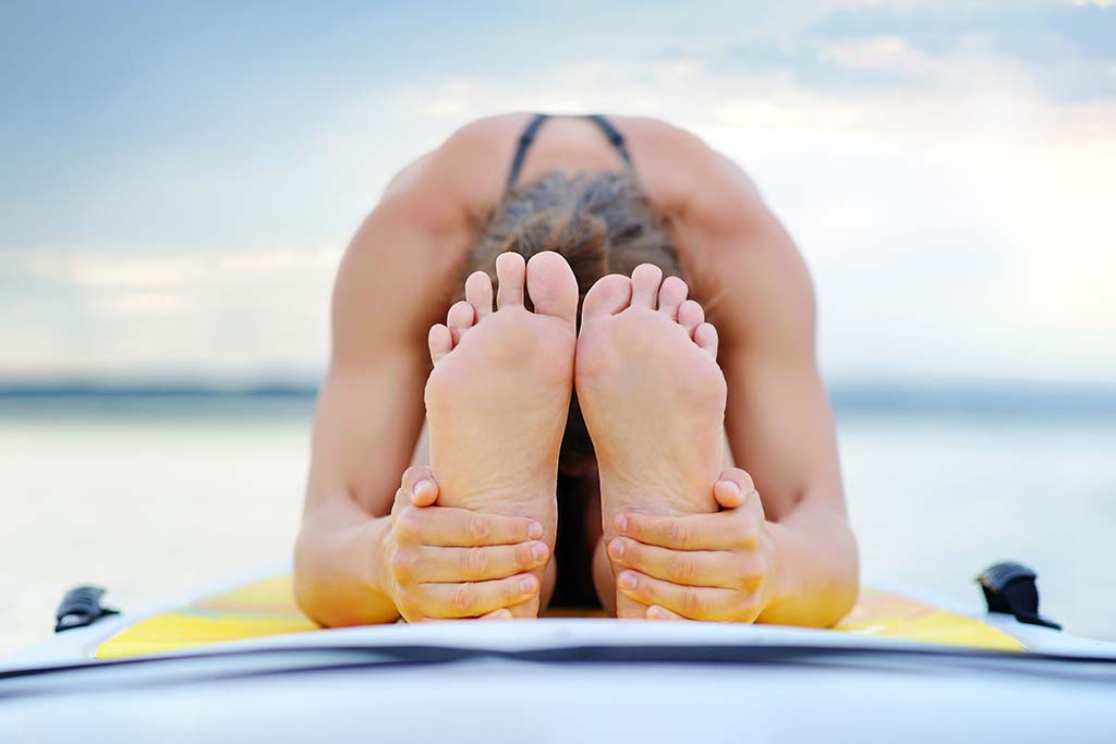 A girl sitting and stretching her legs on an all rounder stand up paddleboard