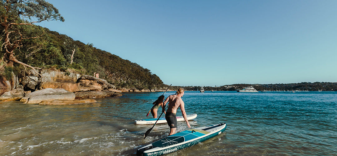 A beautiful beach view with a man and woman hitting the waters to go standup paddleboarding