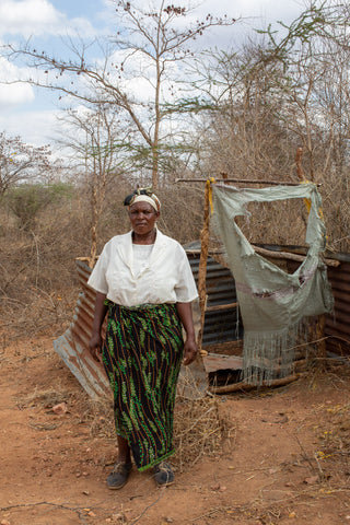 A woman standing in front of a poor pit latrine