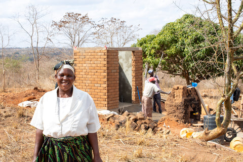 A  woman standing in front of a construction sight of a dry toilet smiling