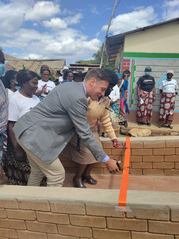 A man and a woman cutting the ribbon amongst artisan women in rural Makueni