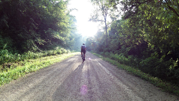 Man riding a bike on a gravel road surrounded by trees