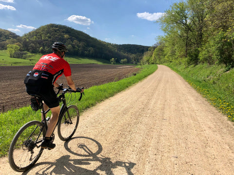 Man riding a bike down a gravel road on a sunny day.