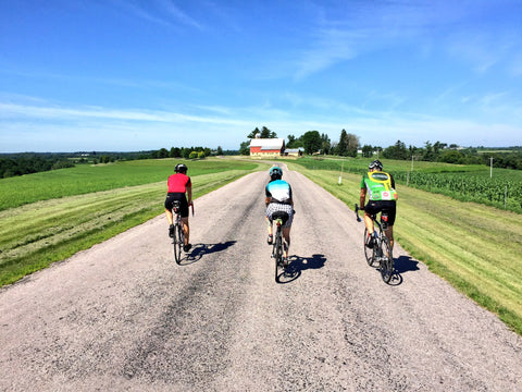 Three people biking on a gravel road surrounded by farmland.