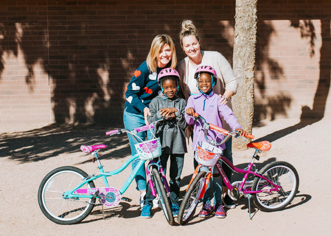 Students Harmony and Heaven taking a photo with their teachers while holding their kids bicycles and wearing their kids bike helmets.