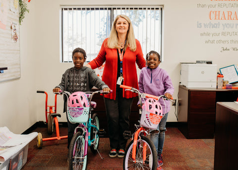 Students Harmony and Heaven taking a photo with their principal while holding their kids bicycles and wearing their kids bike helmets.